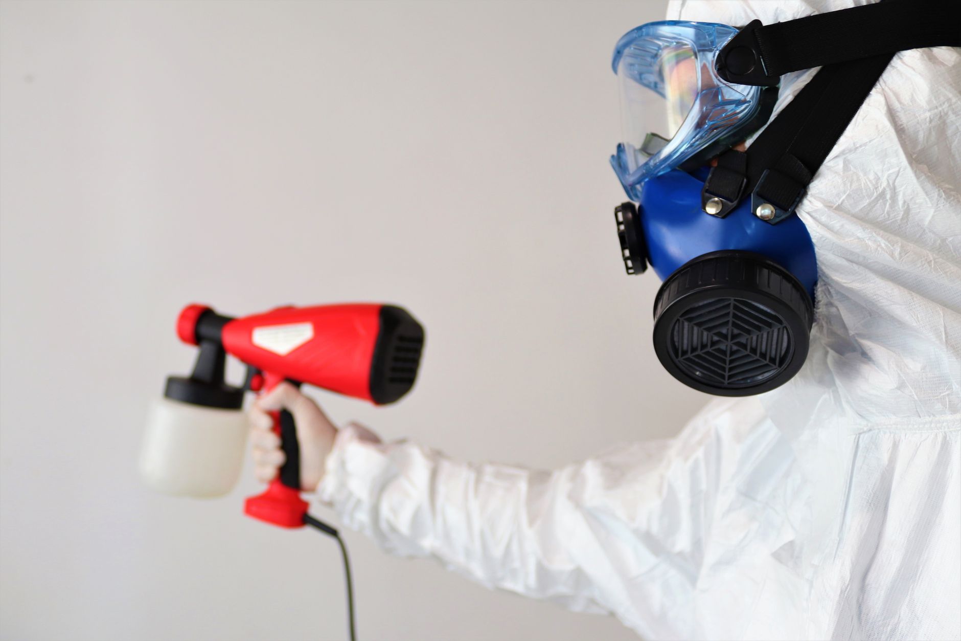 A technician wearing protective gear inspecting a wall for mold in a Crowley, Texas home, with specialized equipment visible.